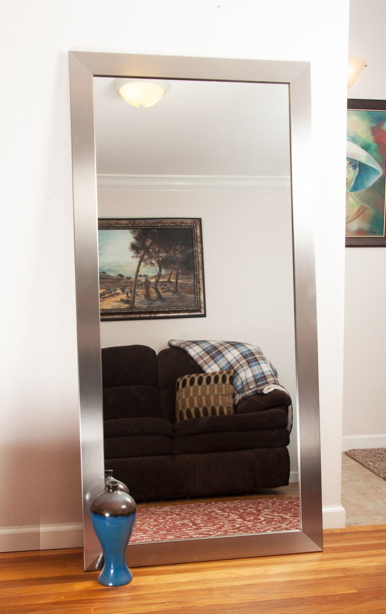 آینه بزرگ تکیه داده شده به دیوار باقاب نقره ای رو به مبل قهوه ای